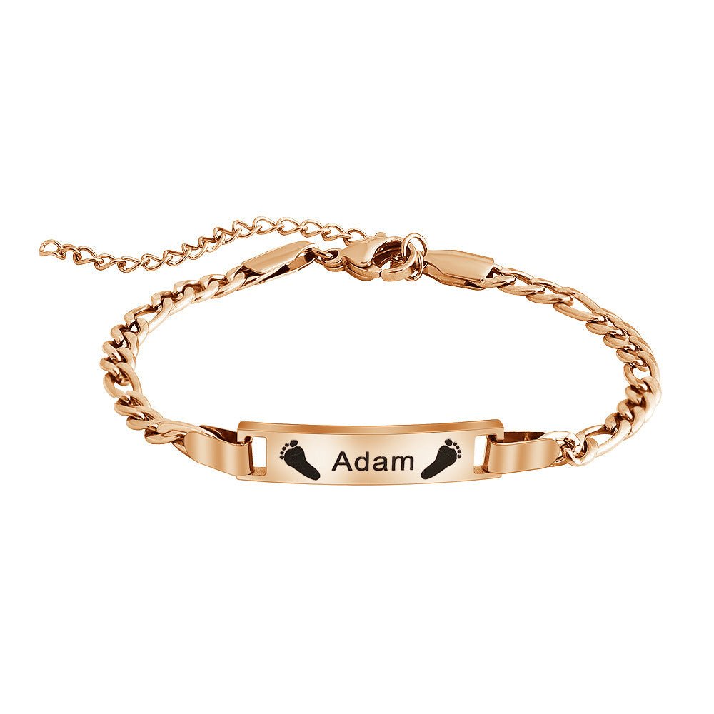 Bracelet naissance en acier doré, maille gourmette fine, plaque gravée prénom Adam avec empreintes de pieds noirs.