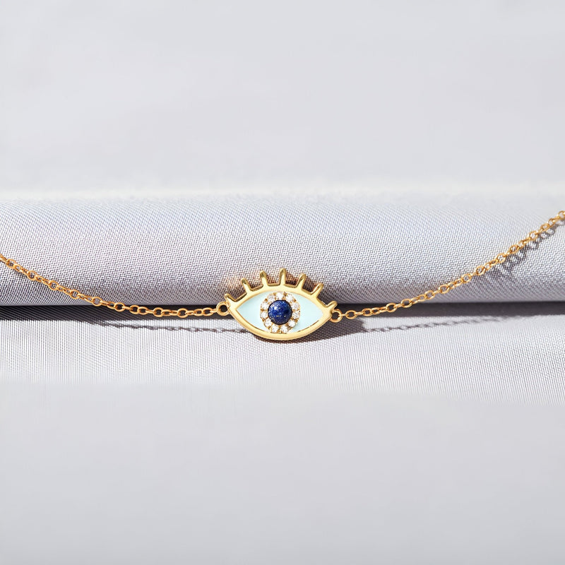 Bracelet femme en or avec pendentif œil serti d'une pierre bleue centrale et détails cloutés sur la paupière.