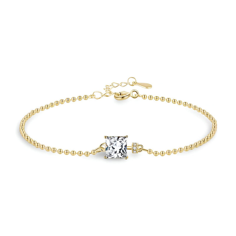 Bracelet fin en argent doré avec chaîne à petites billes et pierre carrée translucide centrale.