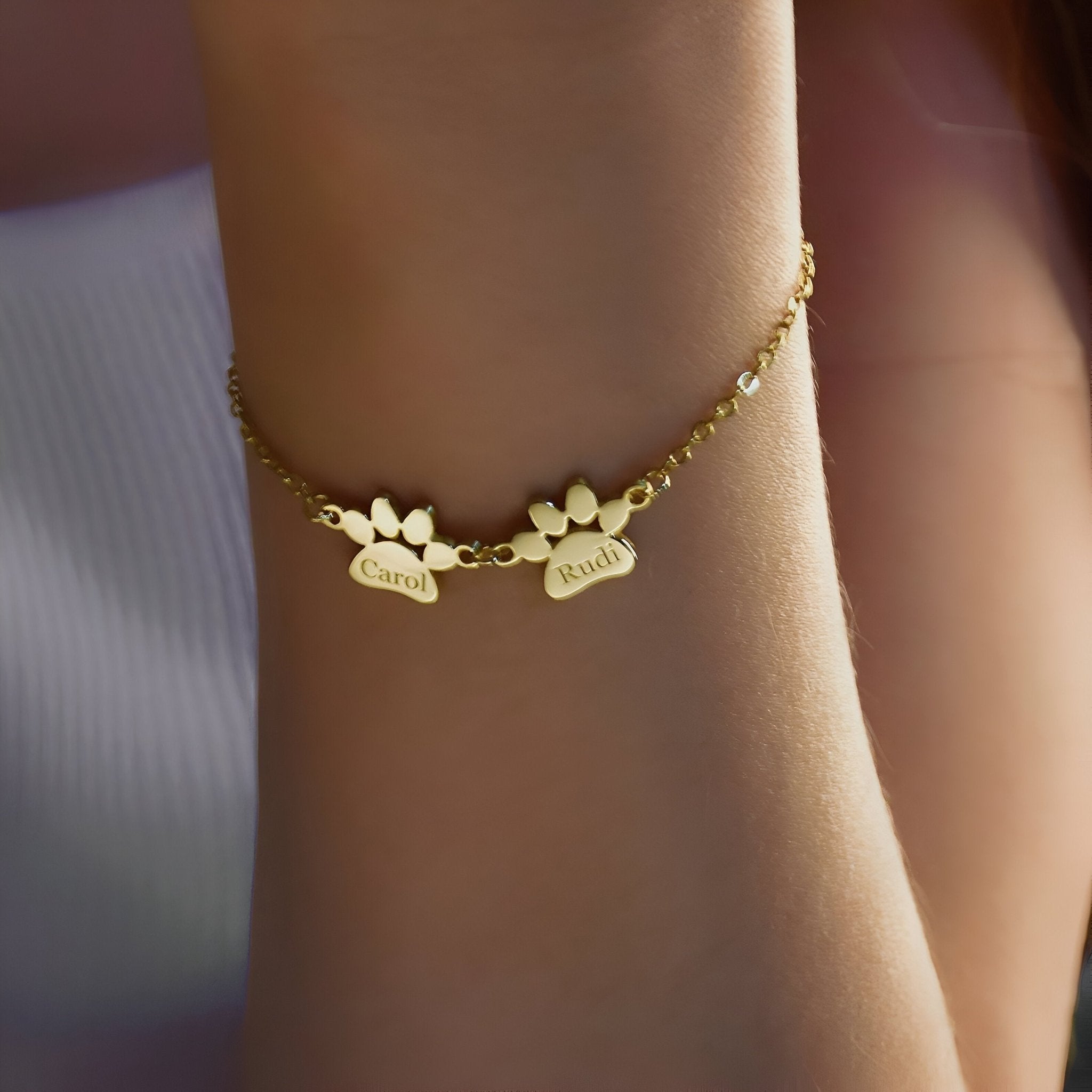 Bracelet fin en acier inoxydable doré avec deux pendentifs pattes personnalisés gravés Tinou, porté au poignet.