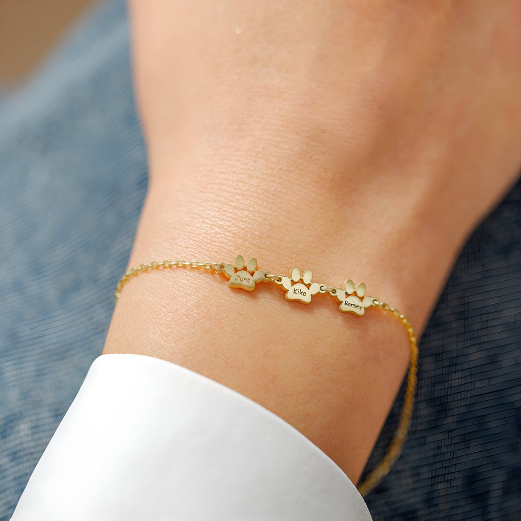 Bracelet fin en acier inoxydable doré avec trois pendentifs pattes élégants ajustable au poignet.