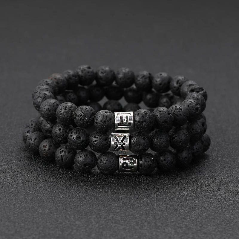Bracelet élastique double rang en perles noires de pierre de lave avec trois breloques argentées gravées de symboles.