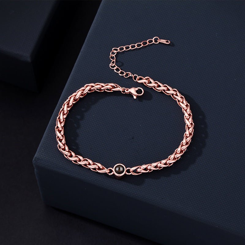 Bracelet maille tressée en acier inoxydable rose doré avec fermoir réglable et détail rond noir au centre.