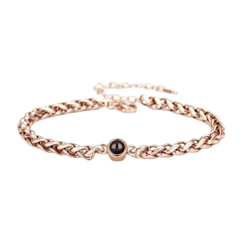 Bracelet maille tressée en acier inoxydable couleur or rose avec perle noire centrale et fermoir réglable.