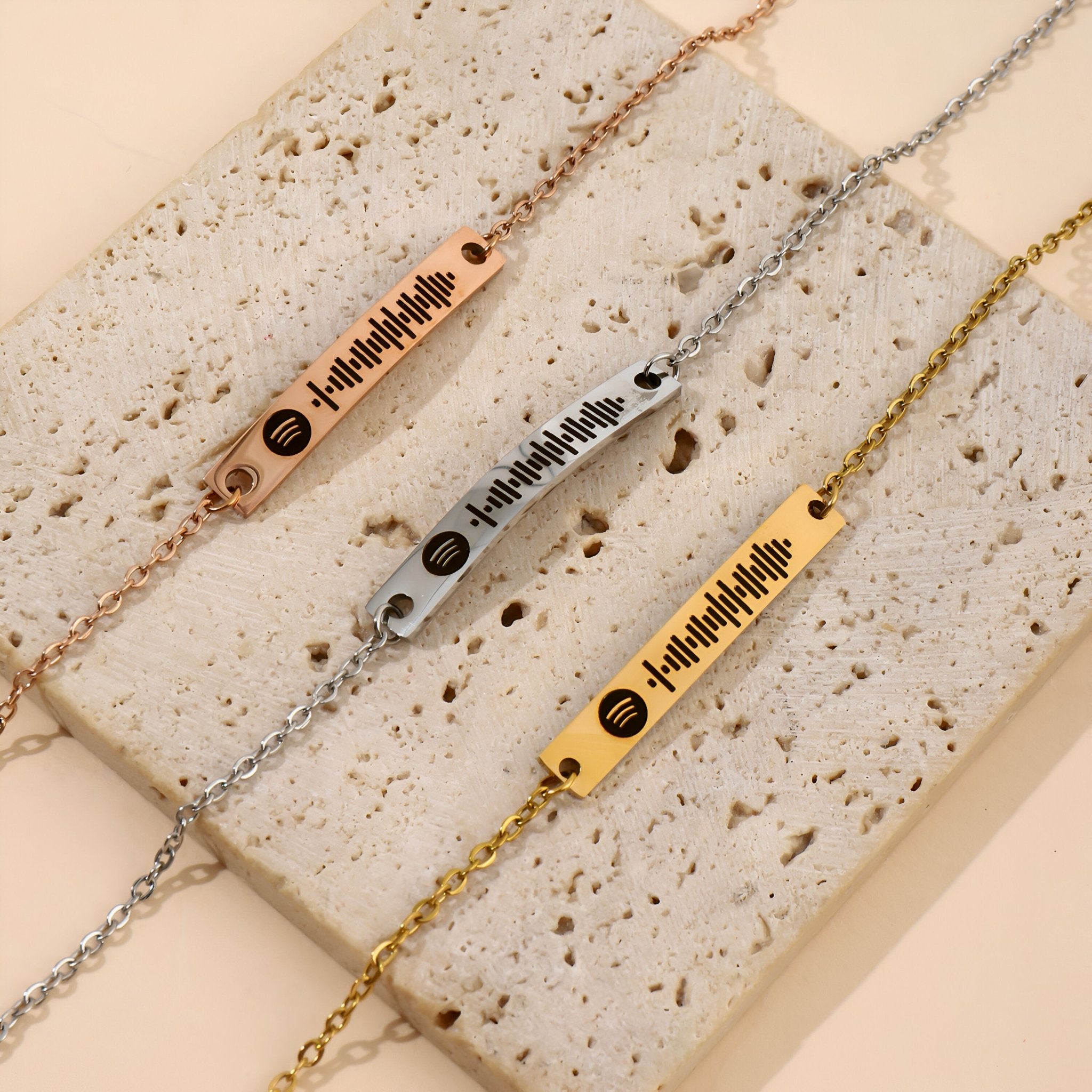 Trois bracelets gourmettes ajustables avec plaques Spotify en or rosé, argent et or, sur fond beige.