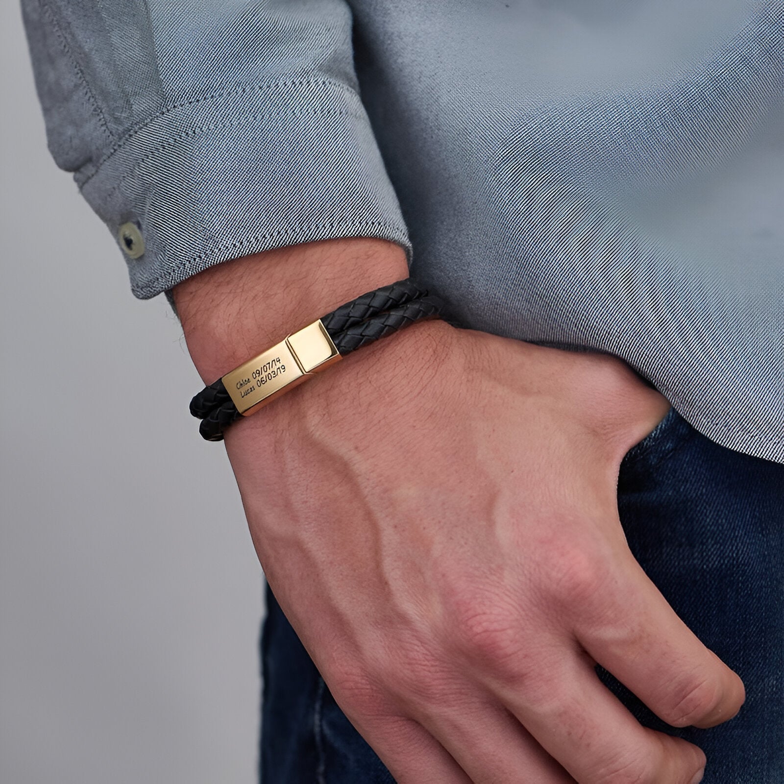 Bracelet double tour en cuir noir tressé avec fermoir plaqué or gravé porté au poignet.