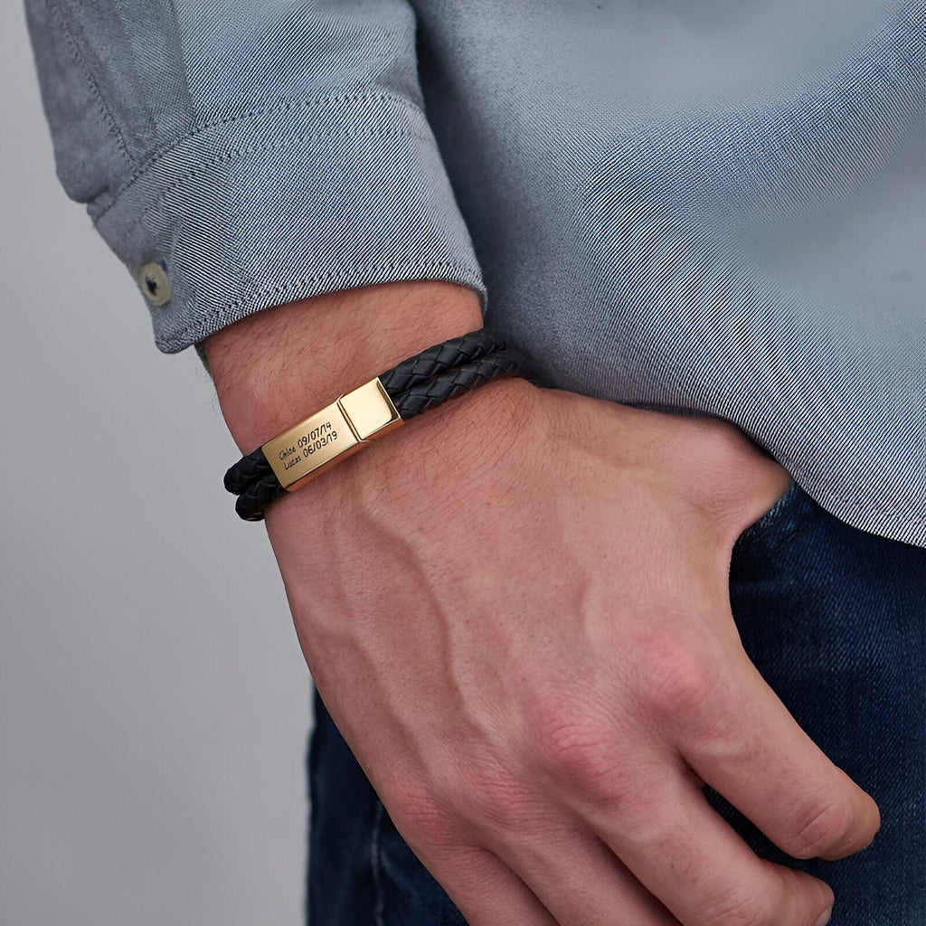 Bracelet double tour en cuir noir tressé avec fermoir plaqué or gravé porté au poignet.