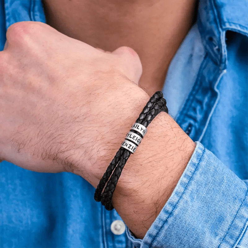 Bracelet triple tour en cuir noir tressé avec trois anneaux métalliques personnalisables porté au poignet.