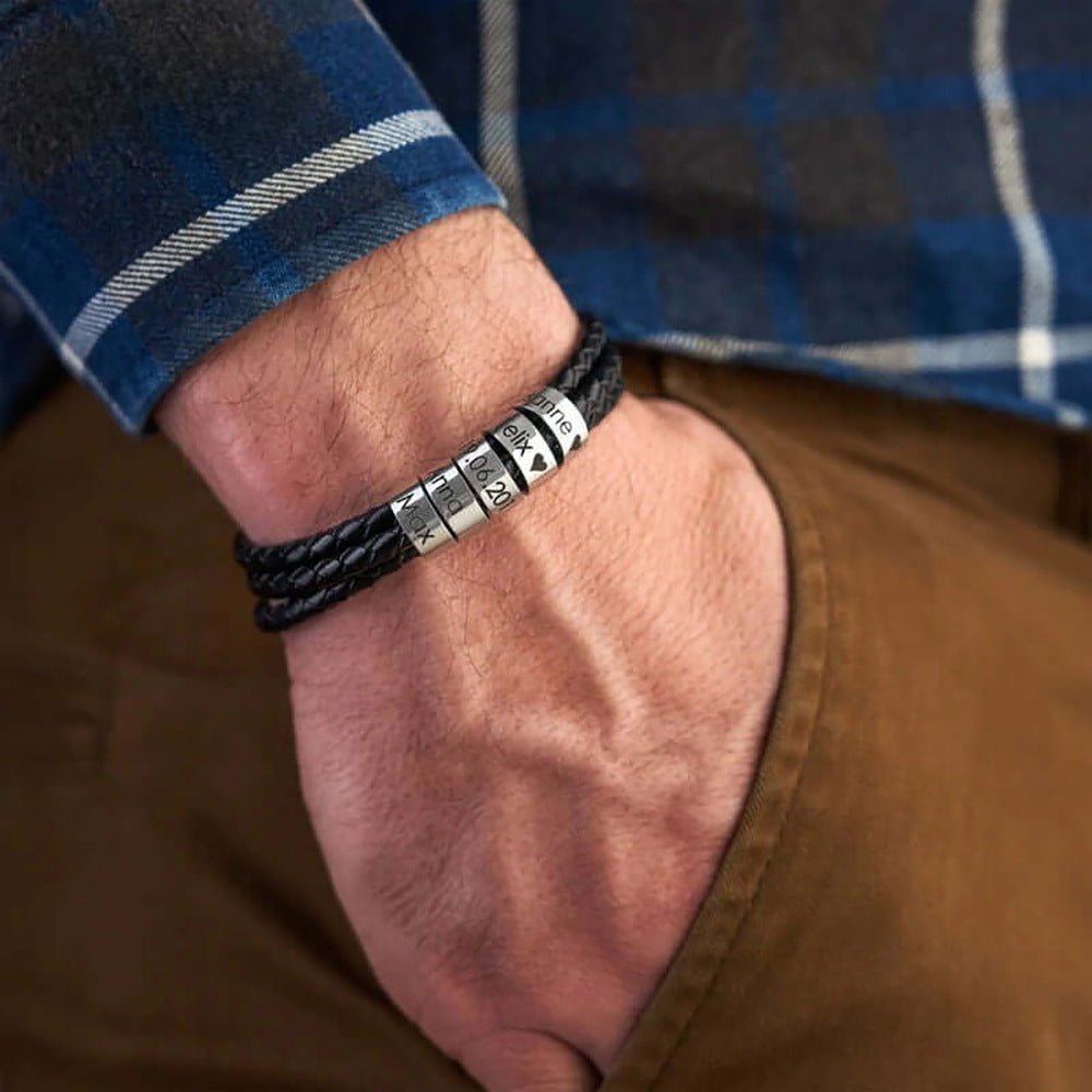 Bracelet en cuir noir tressé triple tour avec cinq anneaux métalliques gravables porté au poignet.