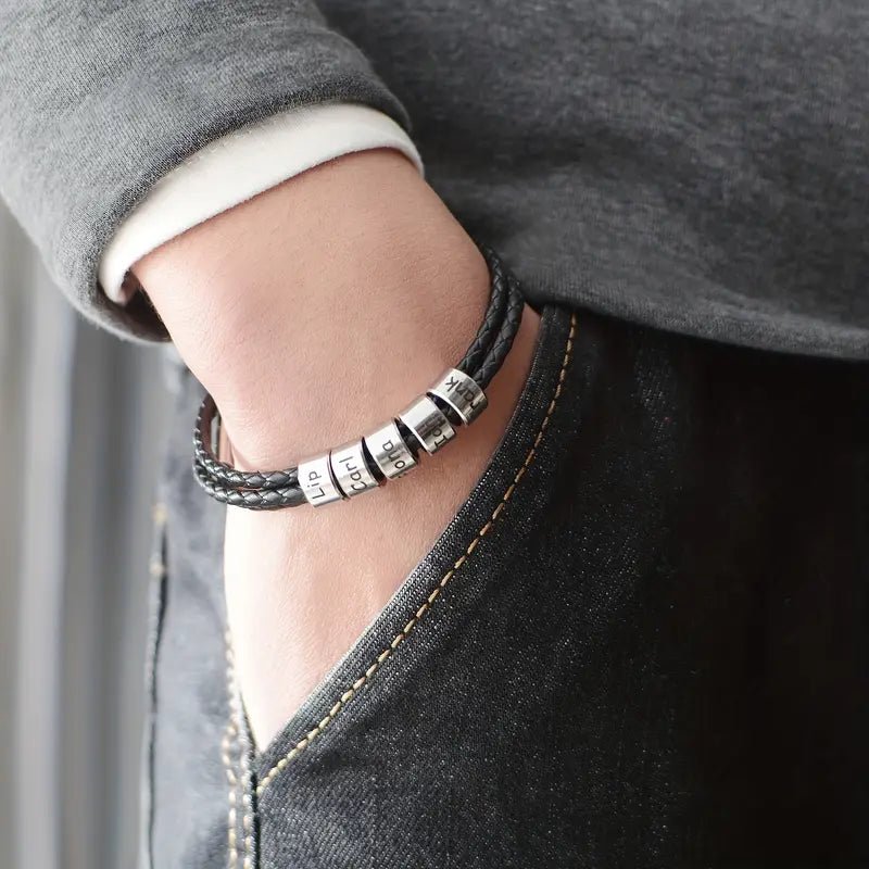 Bracelet en cuir noir triple tour avec cinq anneaux argentés gravables porté au poignet.
