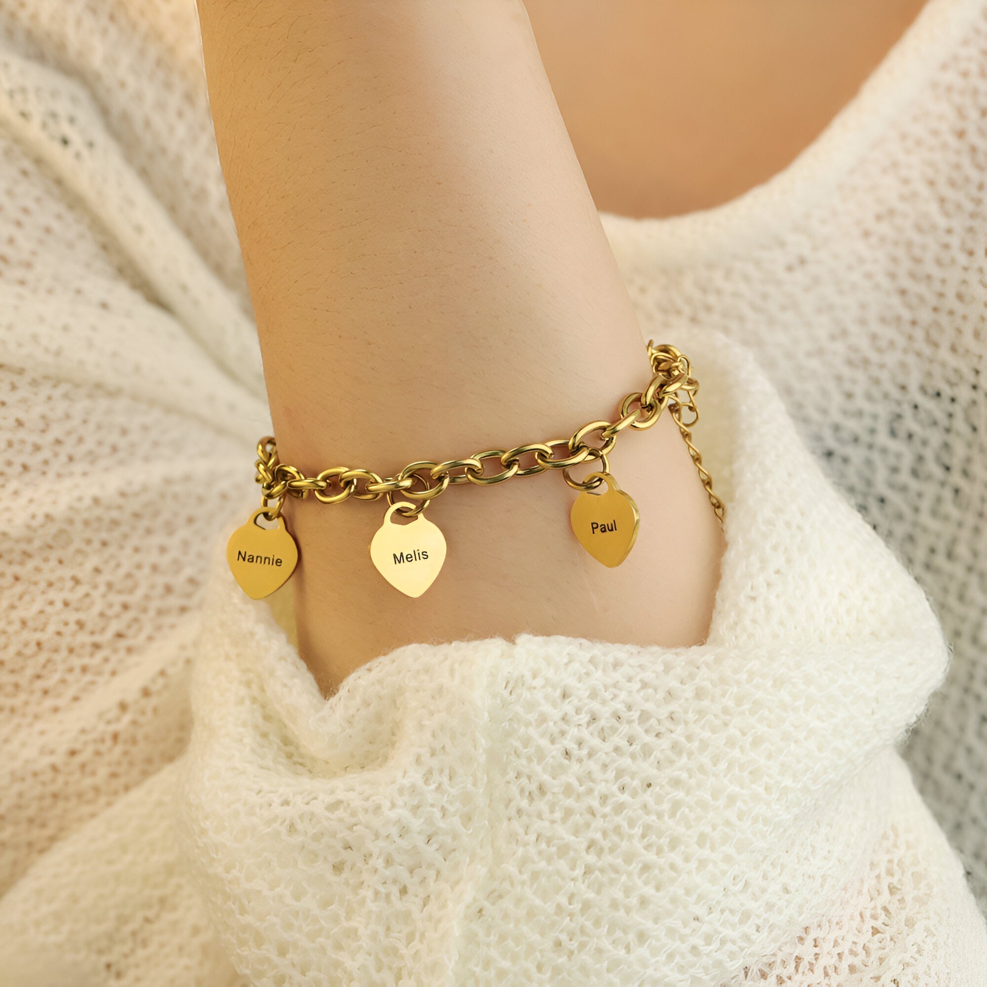 Bracelet en acier inoxydable doré avec cinq plaques en forme de cœur gravées, porté sur poignet féminin.