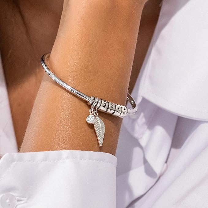 Bracelet en acier inoxydable argenté à quatre anneaux avec pendentif aile et breloque ronde portée sur poignet féminin.