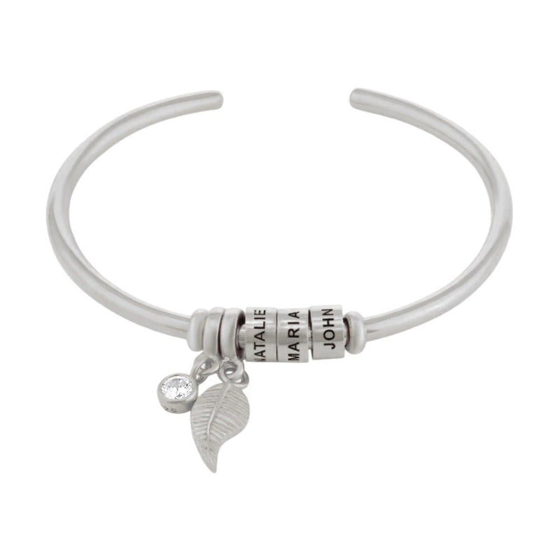 Bracelet ouvert en acier inoxydable argenté avec trois anneaux personnalisables et deux breloques pendantes, dont une.