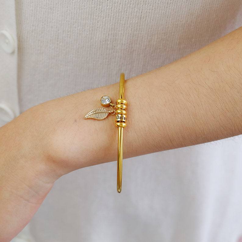 Bracelet fin en acier inoxydable doré avec anneau décoratif et petit pendentif perle sur poignet féminin.