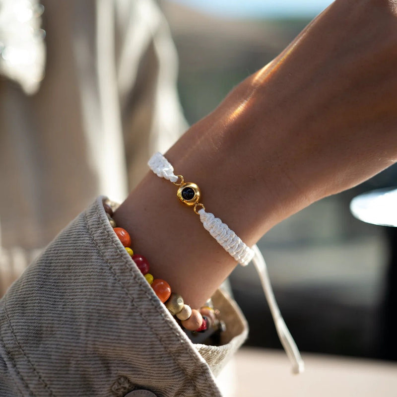 Bracelet fin en corde blanche tressée avec un médaillon rond en titane doré personnalisable, porté au poignet.