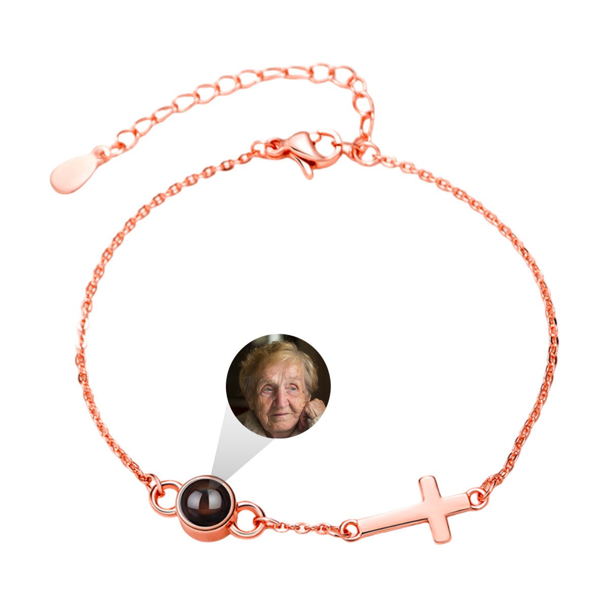 Bracelet fin en acier inoxydable rose avec croix chrétienne plate et chaîne réglable, orné d'un petit médaillon rond noir.