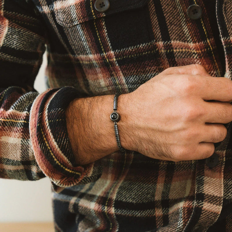 Bracelet fin en pierres heishi noires avec médaillon photo circulaire sur poignet, style naturel et élégant.