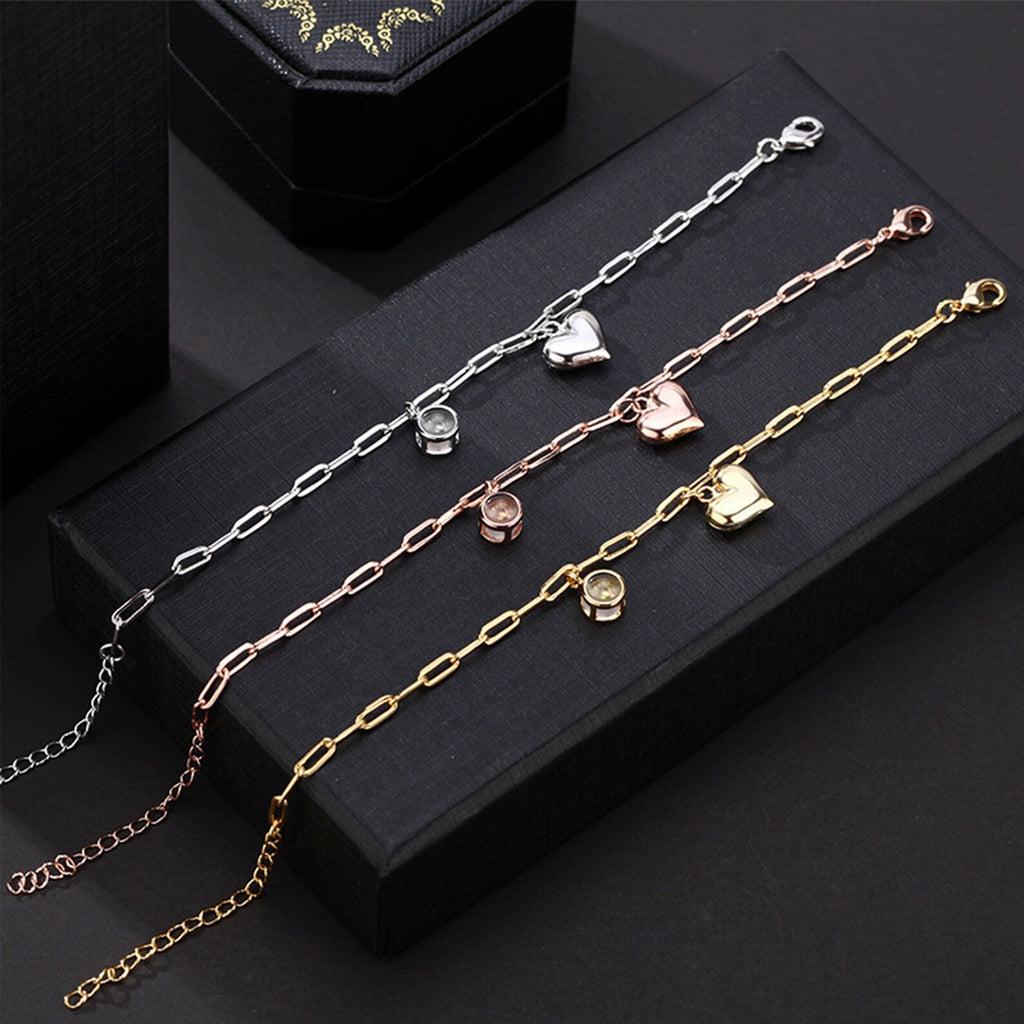 Trois bracelets personnalisés en titane avec charms cœur en or, argent et or rosé sur fond noir.