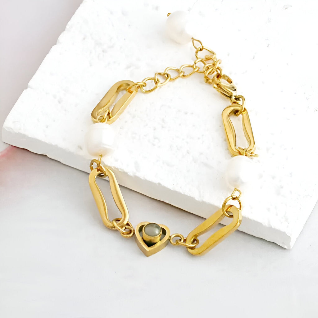 Bracelet en titane doré avec perles d'eau douce et pendentif cœur orné d’une pierre noire.