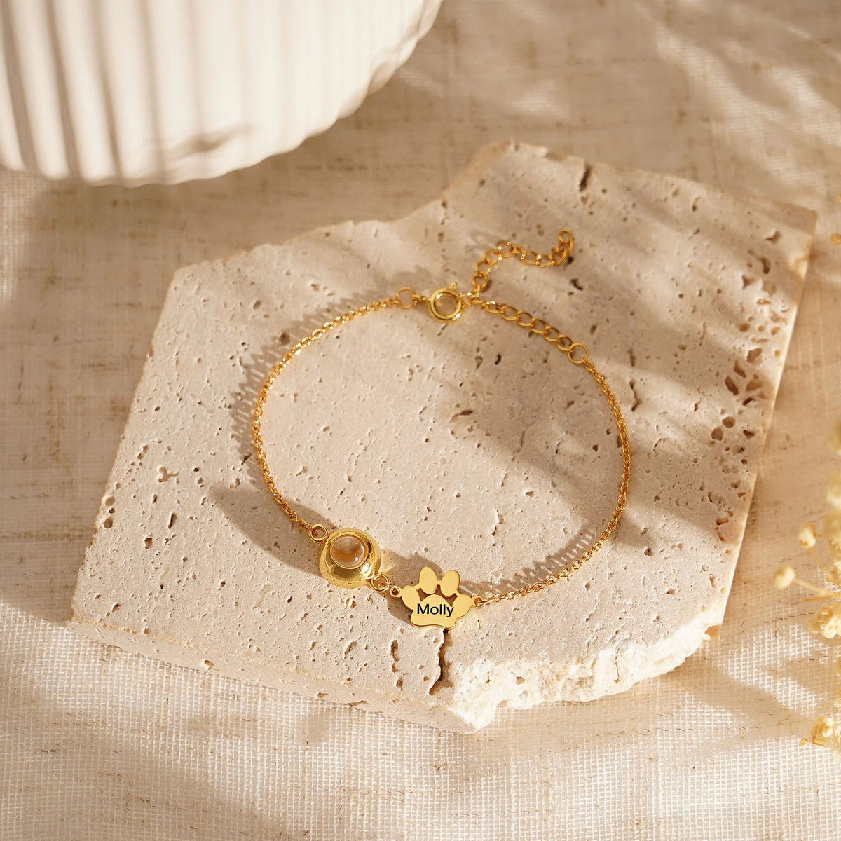 Bracelet personnalisé en acier inoxydable or avec pendentif patte à graver modèle Cliff sur tissu beige texturé.