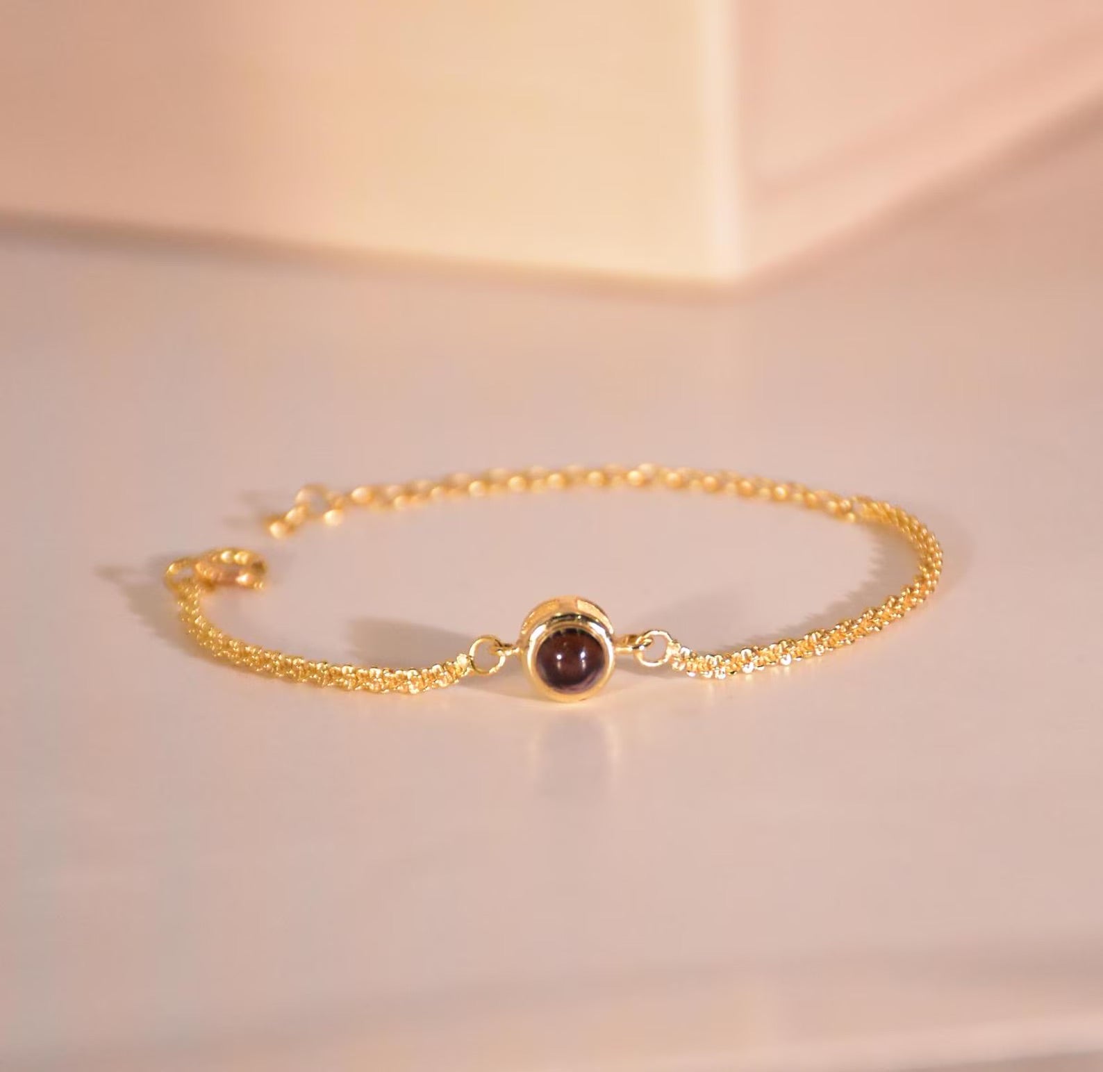 Bracelet fin en acier inoxydable doré avec pendentif rond en projection lumineuse noire, design élégant et minimaliste.