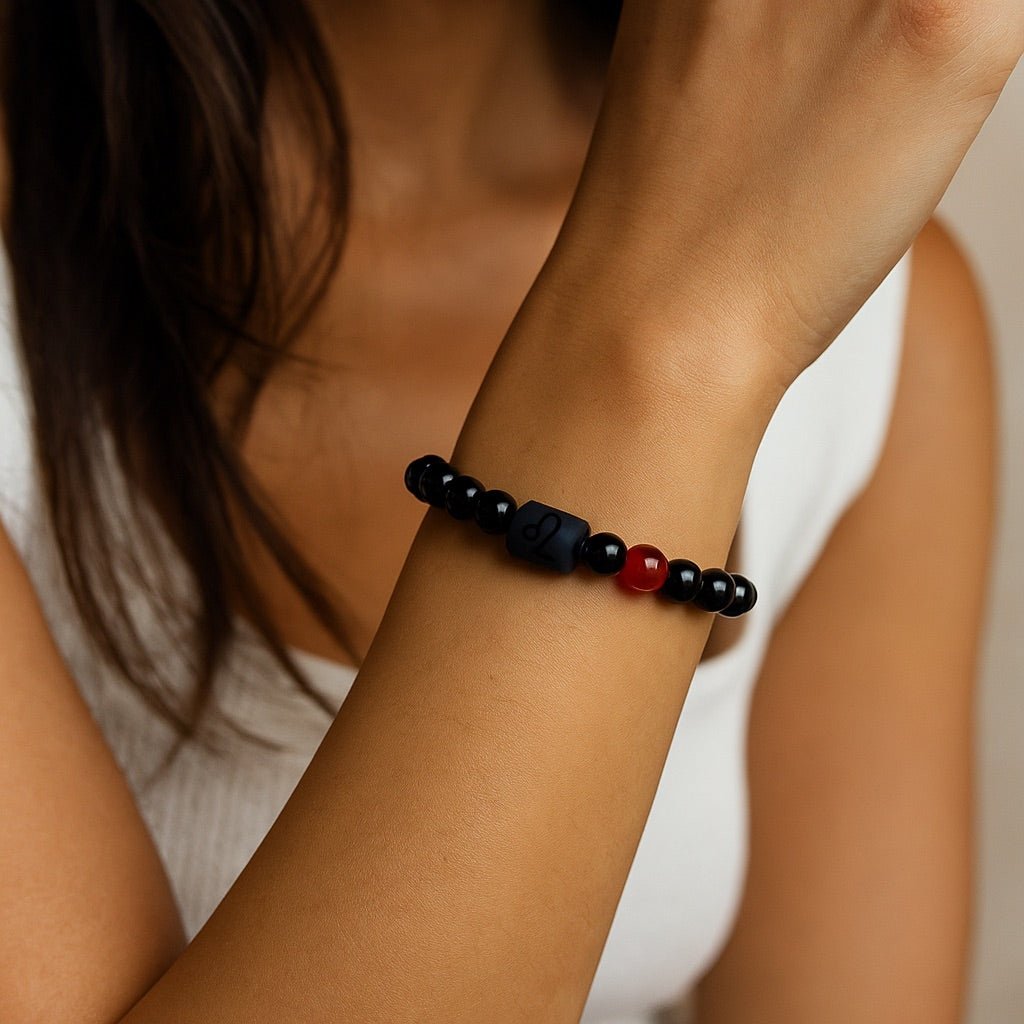 Bracelet en perles de verre noir avec une perle rouge centrale et un symbole astrologique gravé sur une perle noire mate.