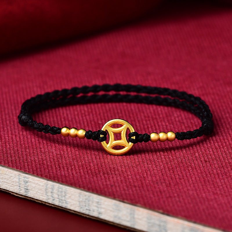 Bracelet fin en fil rouge noir tressé avec pendentif doré rond orné d’un motif ajouré et perles dorées.
