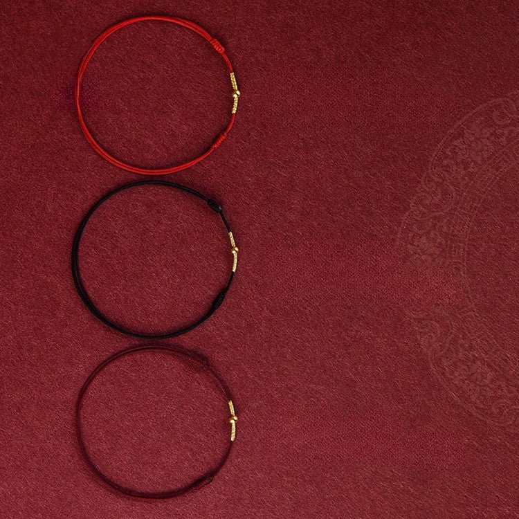 Trois bracelets en fil rouge, noir et bordeaux avec fermoirs dorés, style minimaliste.