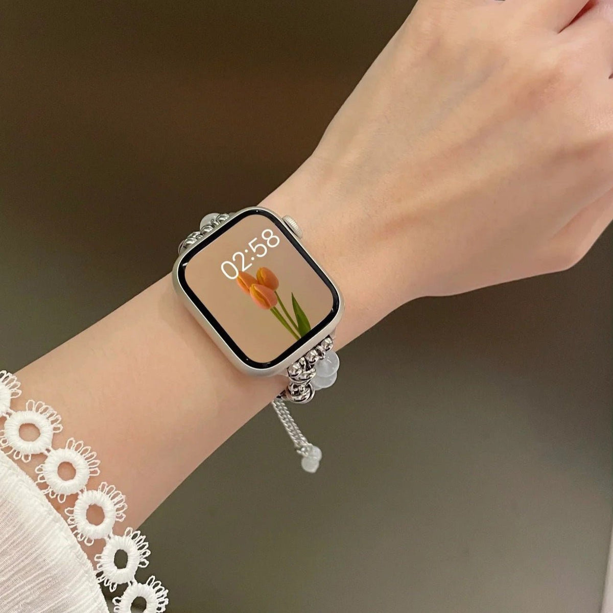 Bracelet ajustable en perles œil de chat blanches et argentées pour Apple Watch portée au poignet féminin.