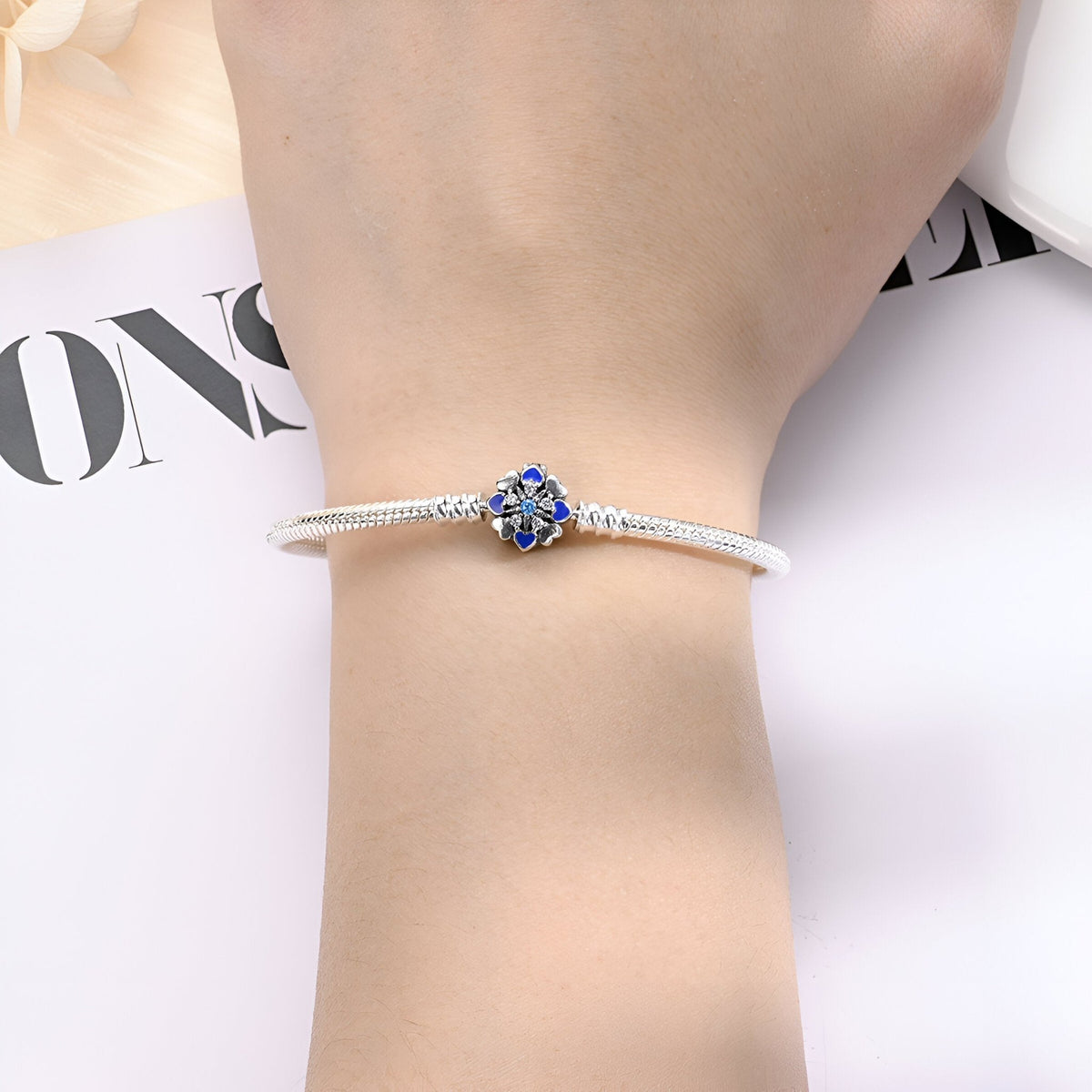 Bracelet argent fin avec charm rond bleu aux détails dorés, porté au poignet féminin.