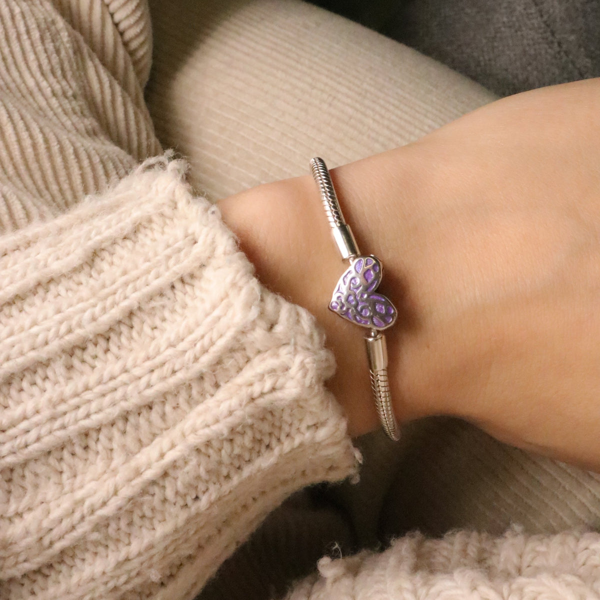 Bracelet argenté fin avec un charm cœur violet lumineux texturé porté sur poignet féminin.
