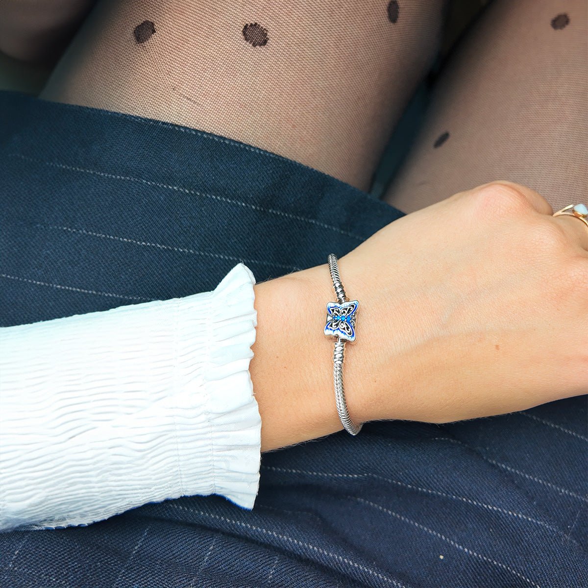 Bracelet fin argenté avec charm en forme de papillon bleu étincelant, porté au poignet féminin.