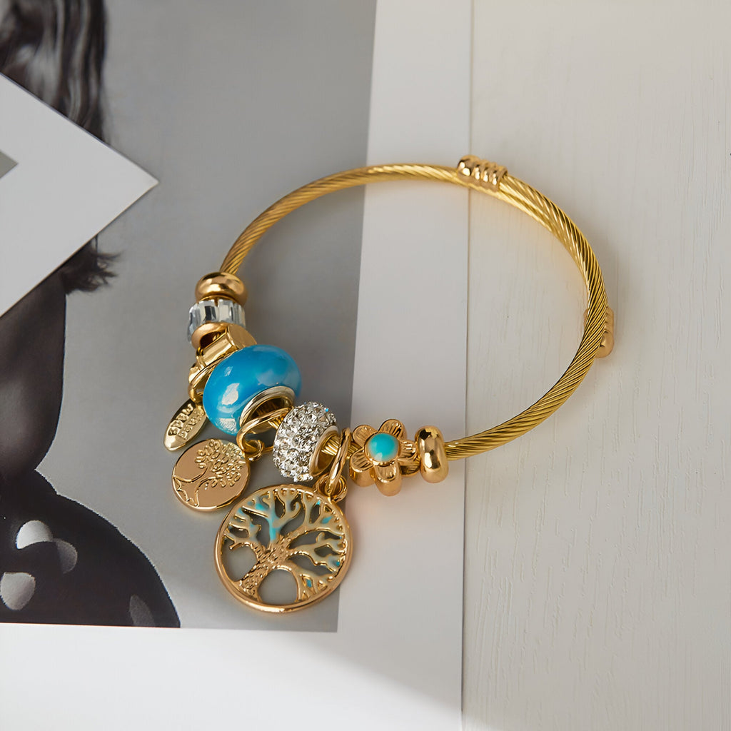 Bracelet or en acier inoxydable avec pendentif arbre de vie et multiples charms turquoise et dorés.