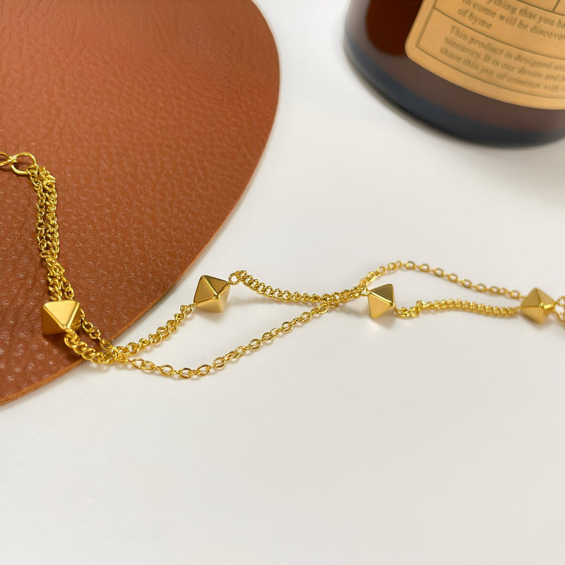 Bracelet femme en acier inoxydable doré avec formes géométriques pyramidales et chaîne fine.