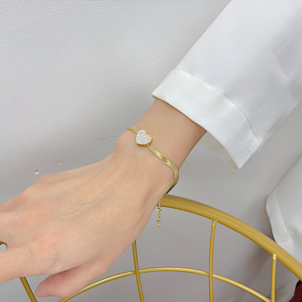 Bracelet fin en acier inoxydable doré avec cœur serti de zirconium porté au poignet féminin.