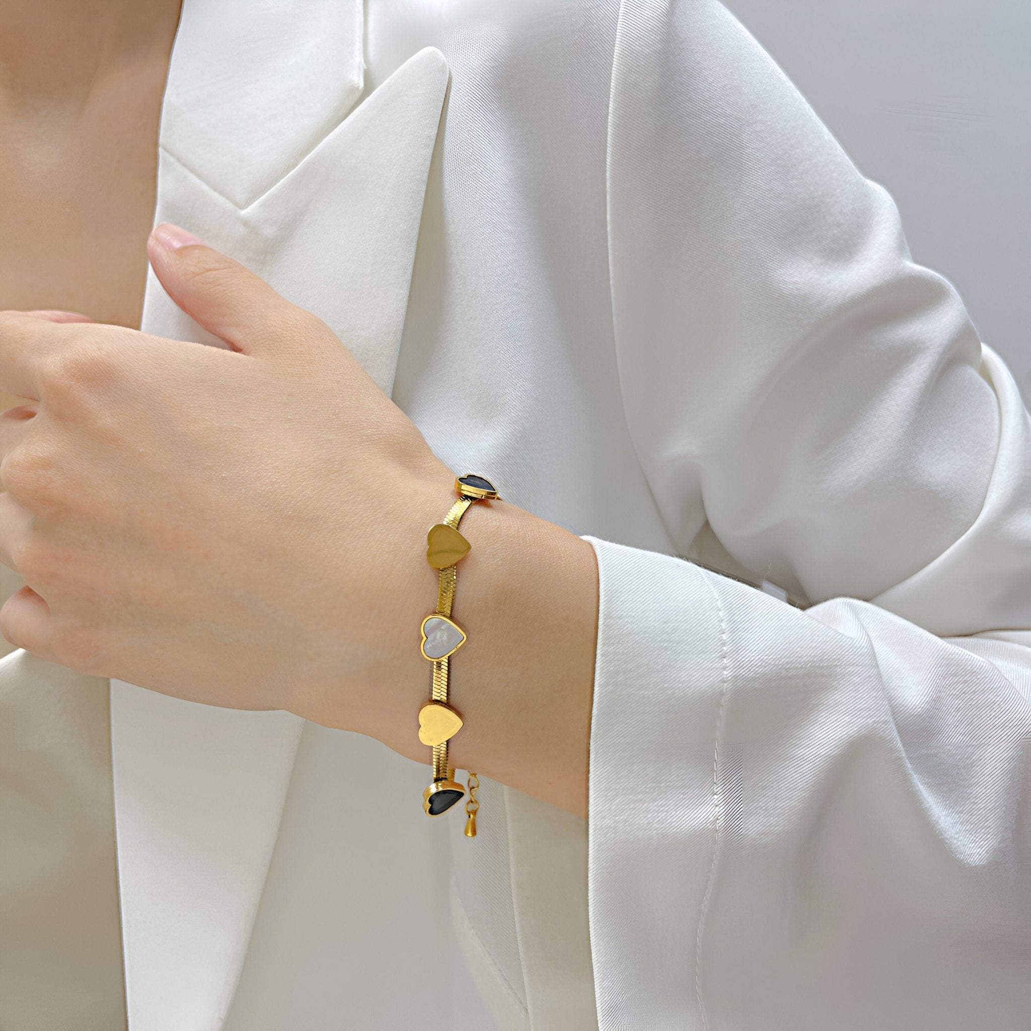 Bracelet en acier inoxydable or avec petits cœurs colorés sur poignet féminin en veste blanche.