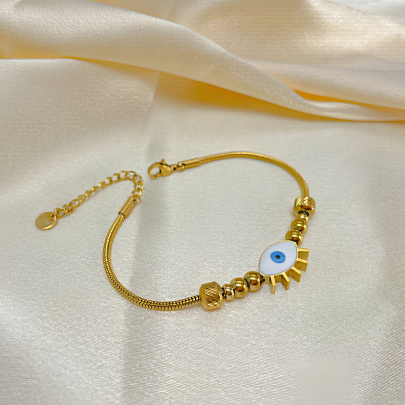 Bracelet femme doré en acier inoxydable avec œil bleu central et pampilles en forme de rayons.