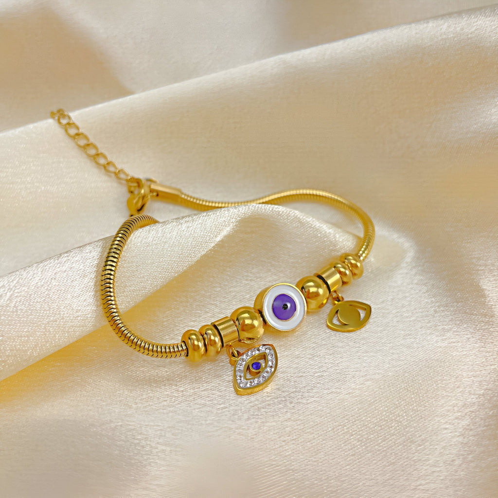 Bracelet en acier inoxydable doré avec œil violet de protection et pendentif cœur serti de pierres transparentes.