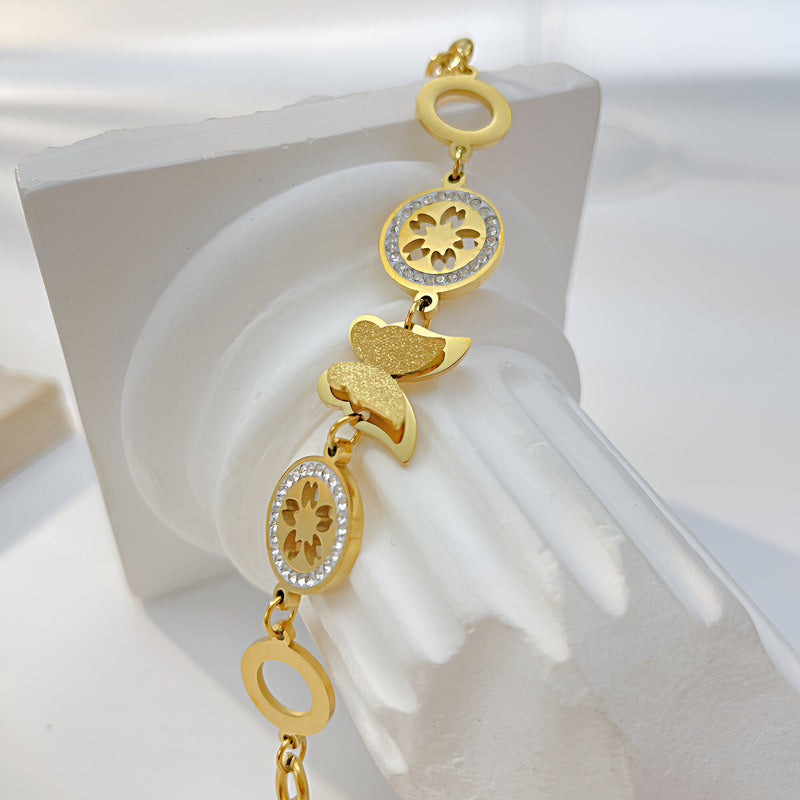 Bracelet femme en acier inoxydable doré avec papillon et éléments floraux ajourés.