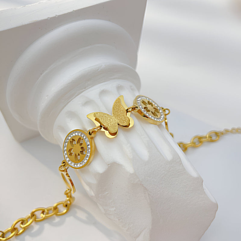 Bracelet en acier inoxydable doré avec papillon et fleurs ornées de petits cristaux.