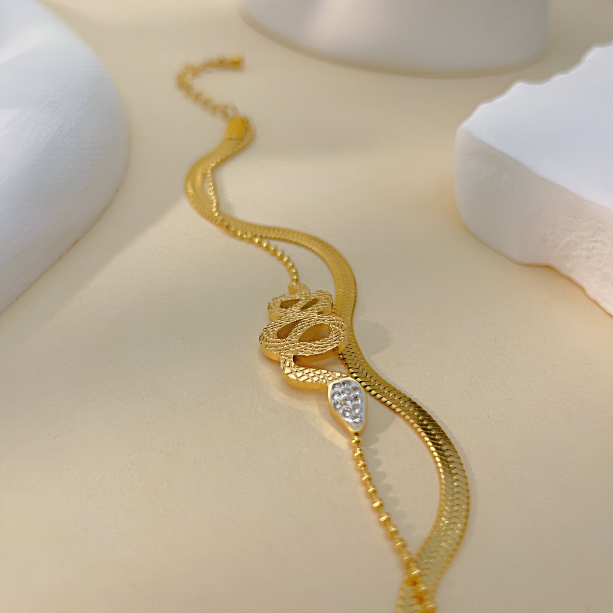 Bracelet or en acier inoxydable à chaîne fine serpent glissant avec détails texturés et tête incrustée de cristaux blancs.