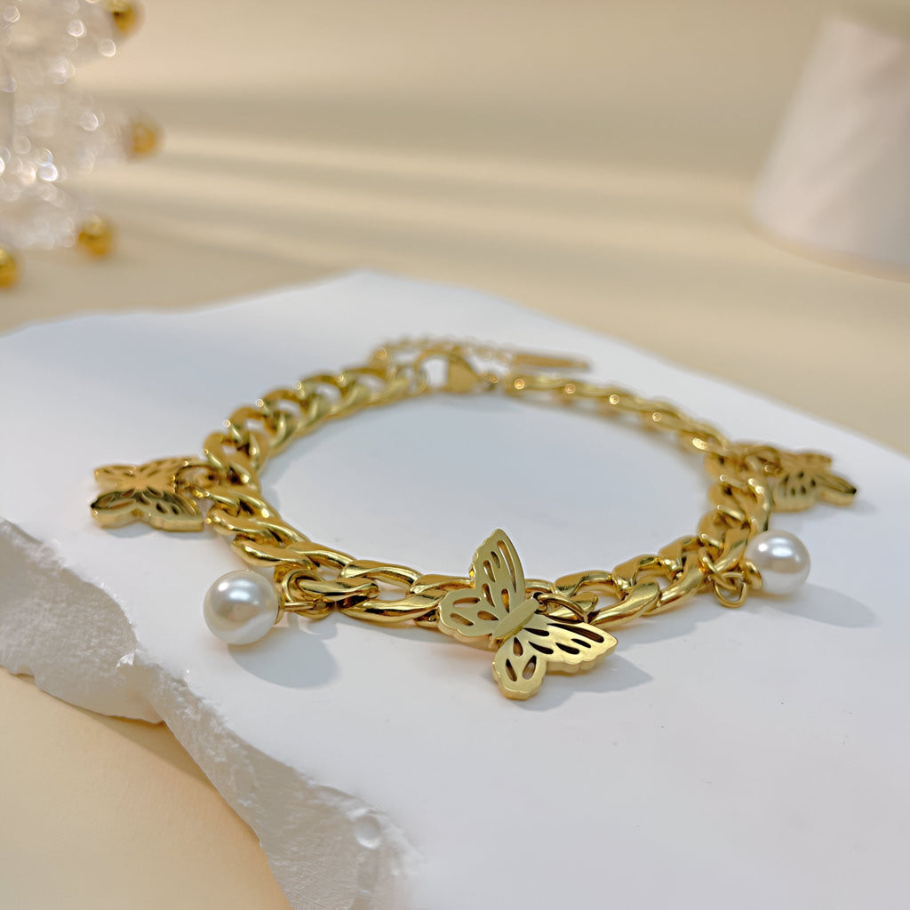 Bracelet femme en acier inoxydable doré avec trois papillons sculptés et perles blanches élégantes.