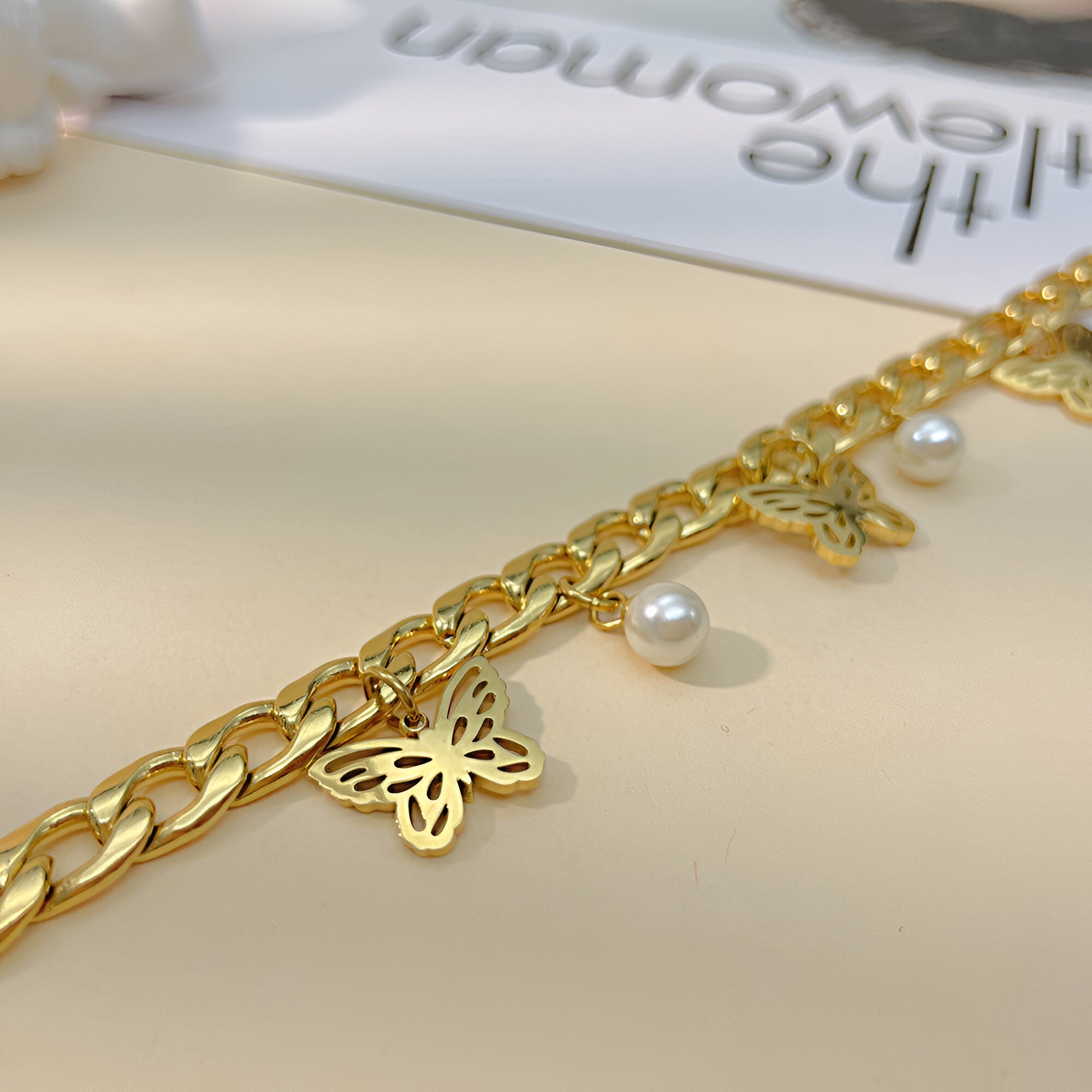 Bracelet or en acier inoxydable avec chaîne large, papillons sculptés et perles blanches élégantes.