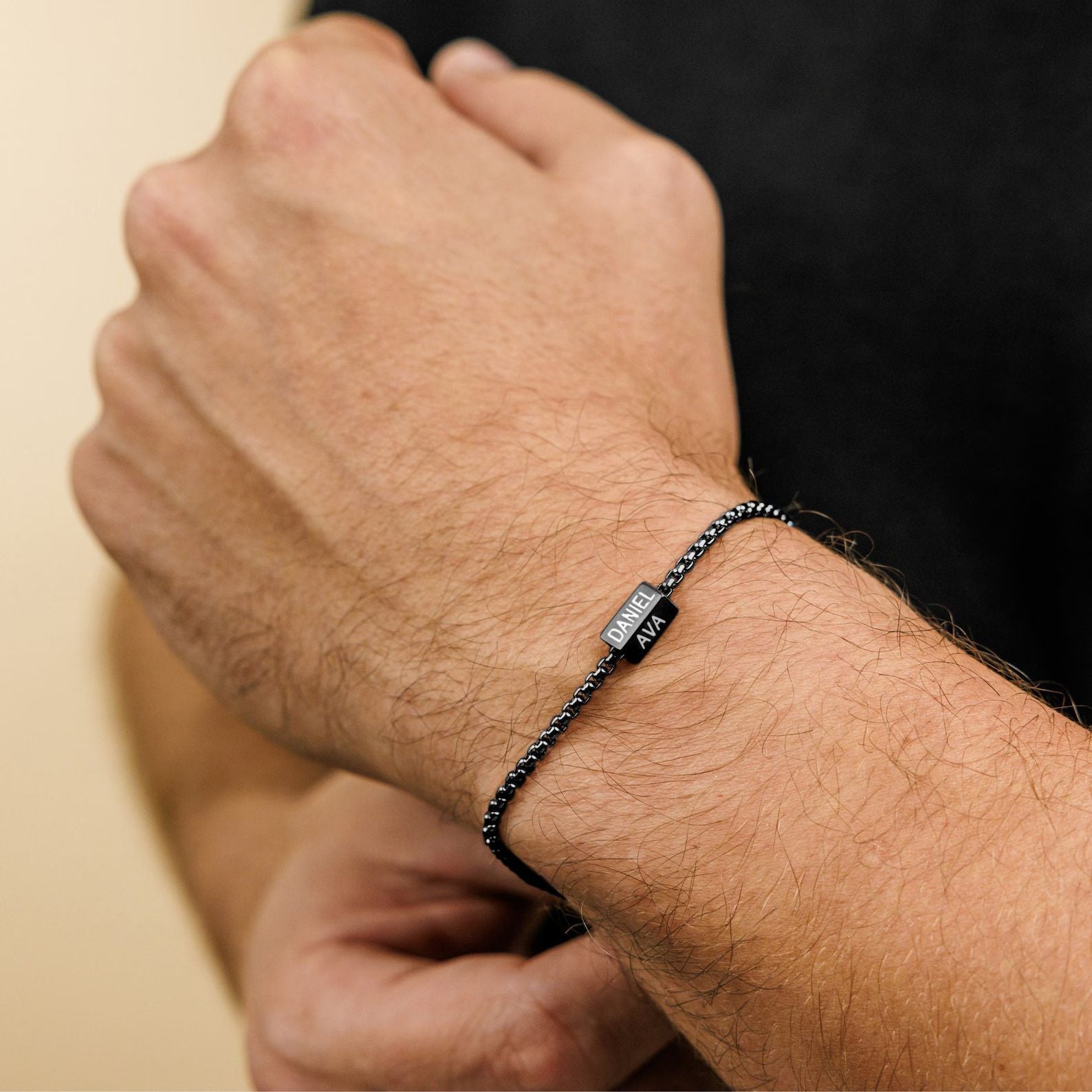 Bracelet prénom personnalisé en acier inoxydable noir, maille vénitienne fine, fermoir sécurisé sur poignet masculin.