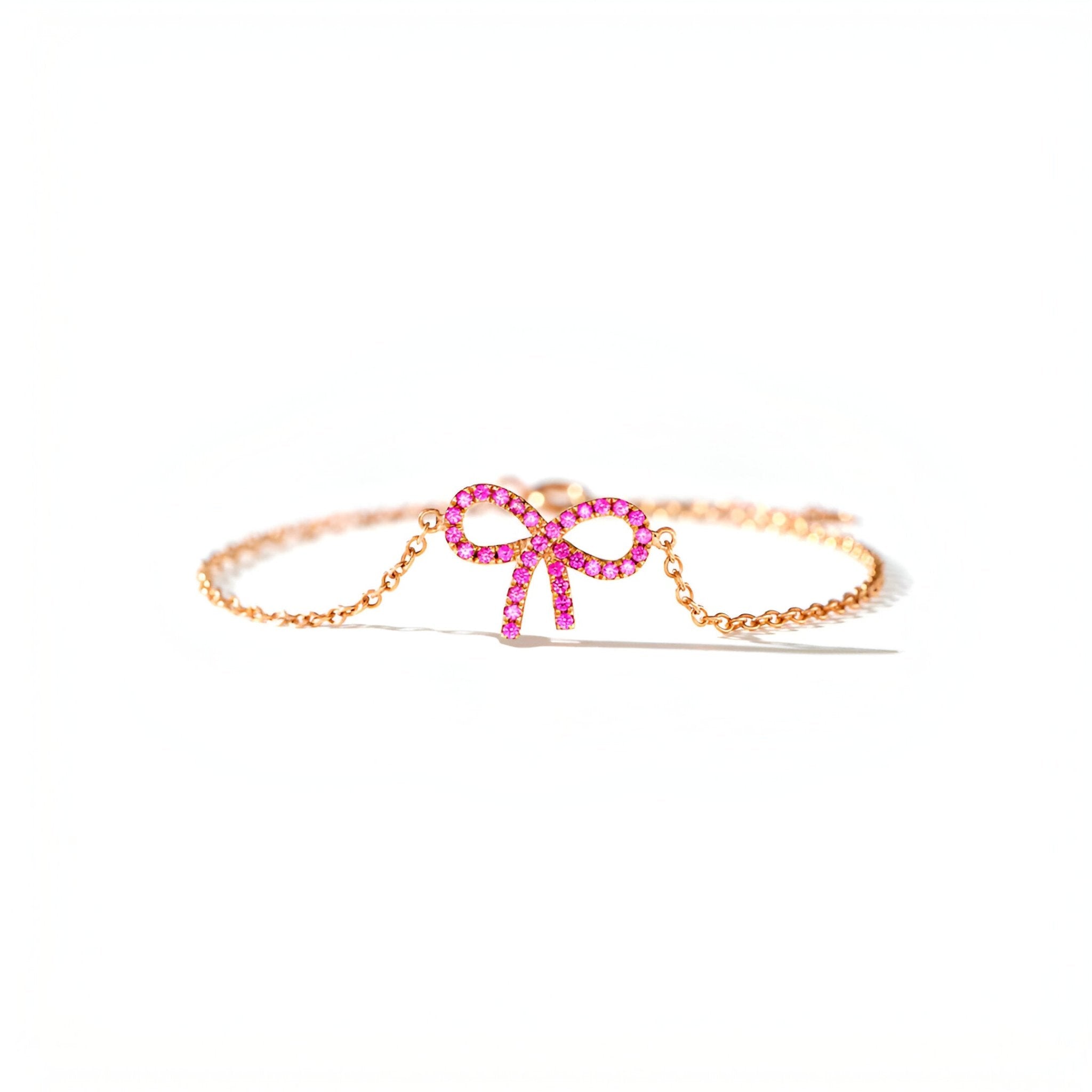 Bracelet en or rosé avec nœud ruban en pierres rose vif et chaîne fine délicate.