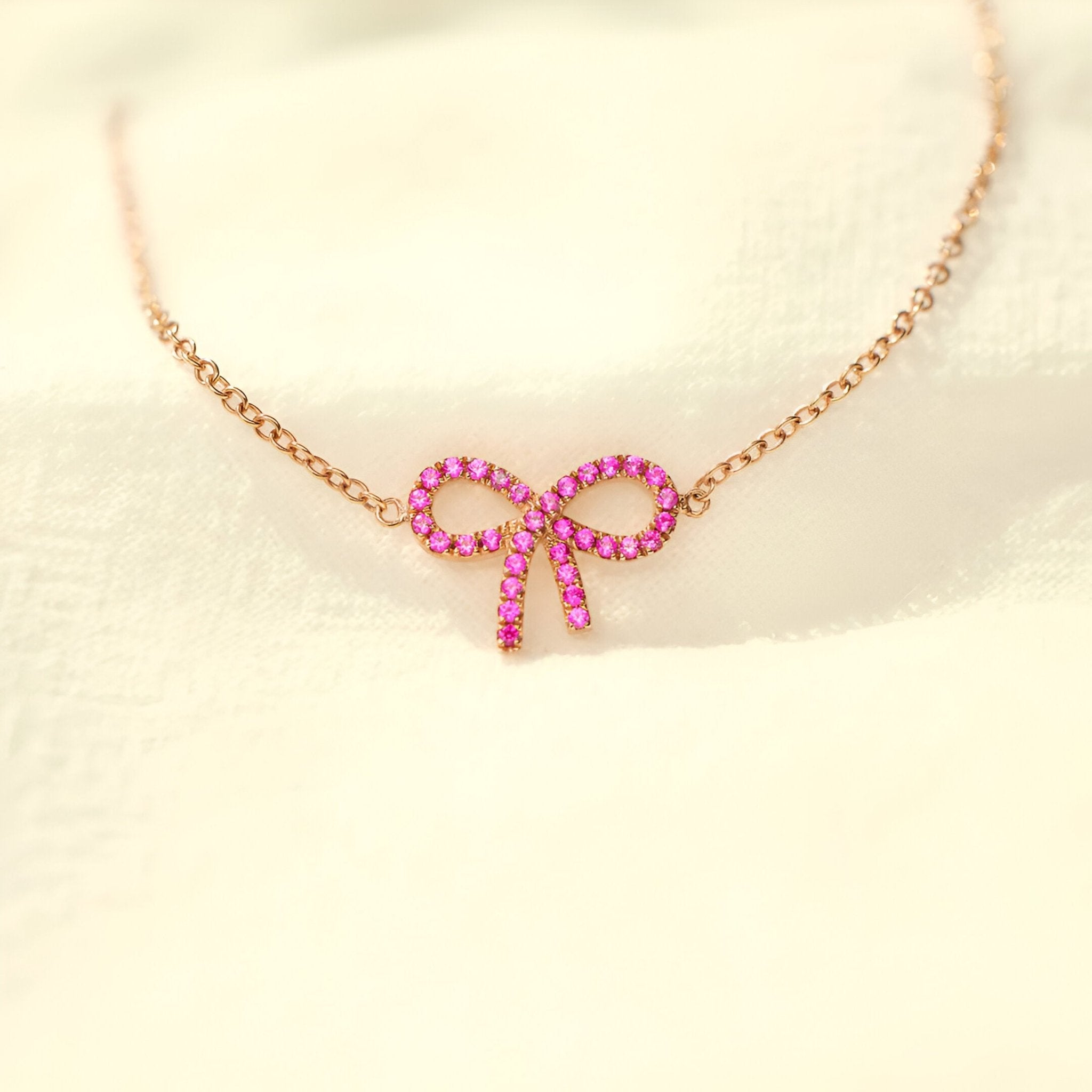 Bracelet fin en or rosé avec pendentif ruban en pierres roses brillantes.