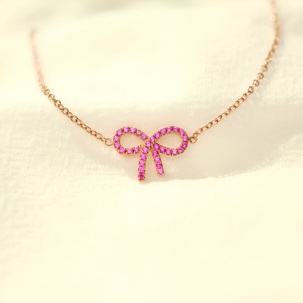 Bracelet fin en or rosé avec pendentif ruban en pierres roses brillantes.