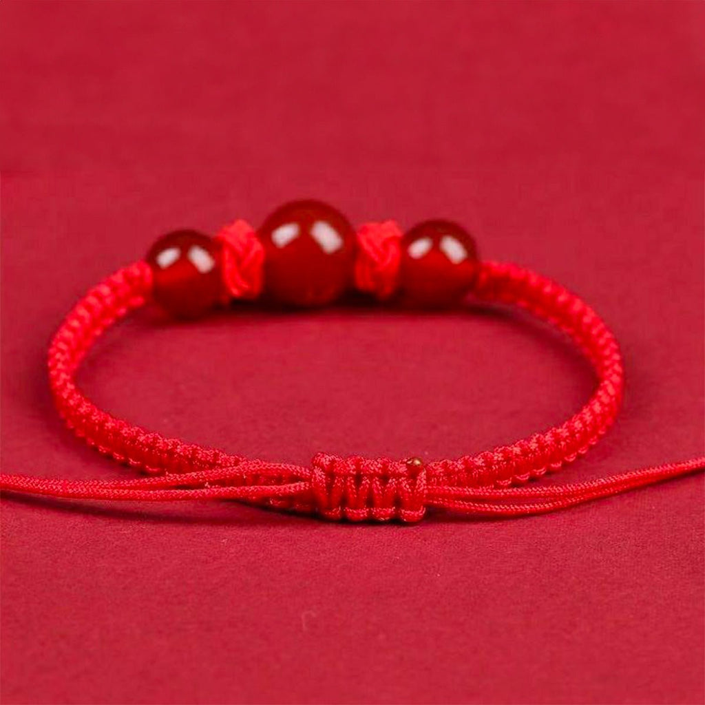 Bracelet en nylon fil rouge avec trois perles rondes rouges et fermeture coulissante tressée.