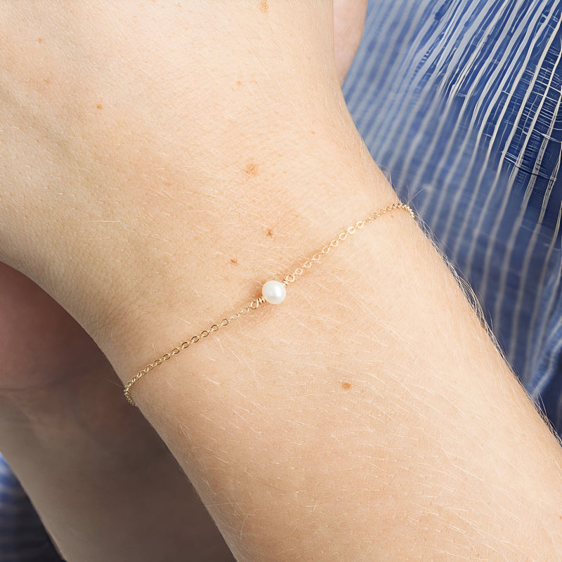 Bracelet fin en acier inoxydable doré avec perle blanche centrale délicate.