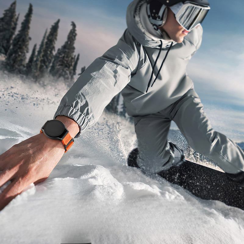 Bracelet sport en nylon orange avec fermoir velcro sur montre connectée noire, porté en snowboard.